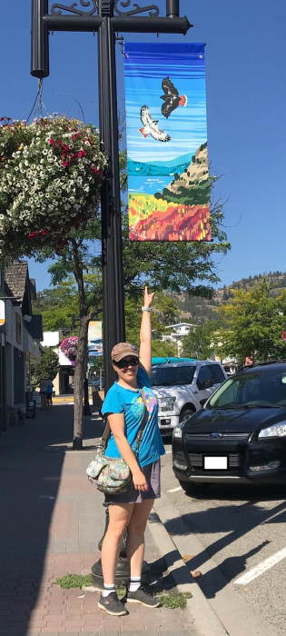 A photo of a woman standing under a vertical banner hanging from a light post.